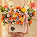 باکس گل رنگارنگ لوکس با رزهای نارنجی، صورتی و زرد، ژربرا، گل‌های سفید و بنفش و روبان صورتی