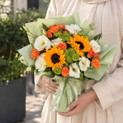 دسته گل آفتابگردان و رز نارنجی آویدا با گل‌های سفید و سبز و کاغذپیچ سبز روشن
