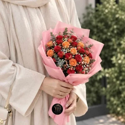 دسته گل رز قرمز و نارنجی مهرا با کاغذپیچی صورتی و گل‌های سفید ریز