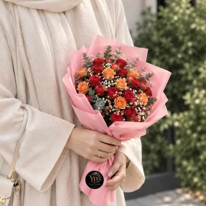 دسته گل رز قرمز و نارنجی مهرا با کاغذپیچی صورتی و گل‌های سفید ریز