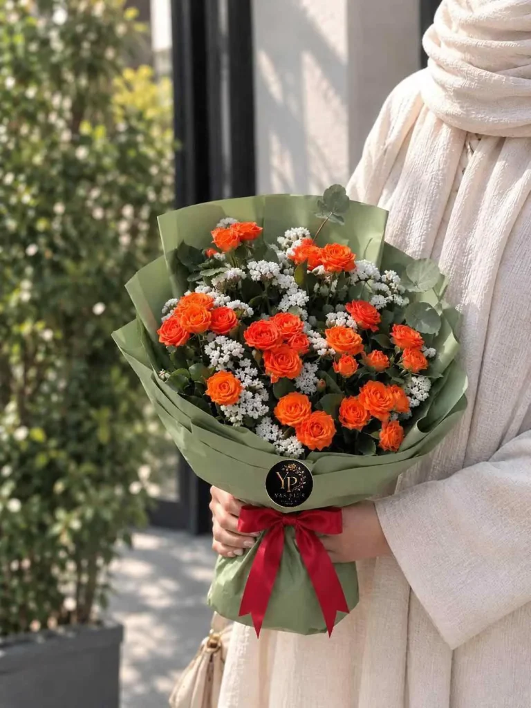 دسته گل رز نارنجی و گل عروس سفید با کاغذپیچ سبز زیتونی و پاپیون قرمز