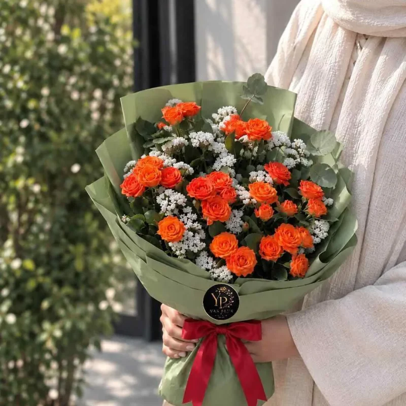 دسته گل رز نارنجی و گل عروس سفید با کاغذپیچ سبز زیتونی و پاپیون قرمز